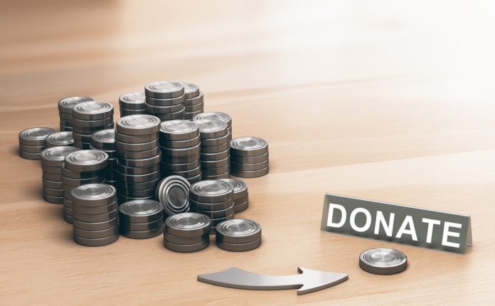 Piles of coins symbols on a wooden table and an arrow pointing a single coin with the word donate. Donation concept. 3d illustration.